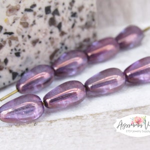 May include: A strand of iridescent purple glass beads with a teardrop shape. The beads are strung on a wire and have a metallic sheen.