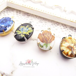 May include: Four oval-shaped porcelain pendants with floral designs. The pendants are in shades of blue, black, brown, and white. Each pendant has a gold or silver metal frame and a loop for hanging.