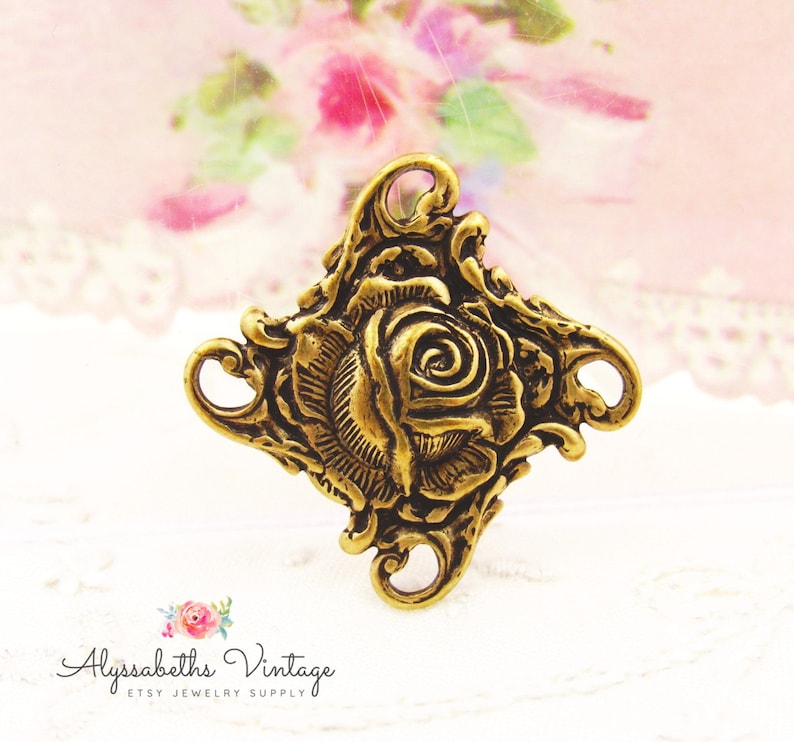 May include: Gold-toned metal charm featuring a raised, detailed design of a rose with ornate scrollwork. The charm has two loops on the sides.