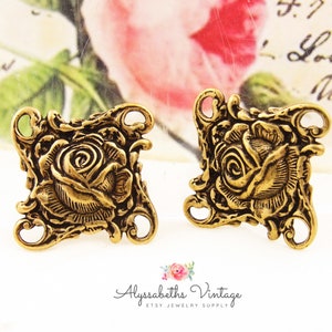 May include: Two gold-tone metal rose charms with four holes for attaching to jewelry or other crafts. The roses are detailed and have a vintage look.