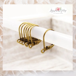 May include: A close-up of six gold-toned earring hooks. The hooks are made of metal and have a simple design. They are displayed on a white surface.