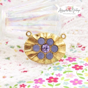 May include: Gold-toned metal pendant with a flower design featuring six purple glass stones and a smaller purple rhinestone in the center. The pendant has two jump rings for attaching to a chain or cord.