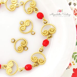 May include: Gold-tone metal jewelry findings with a swirl design. The findings are strung together with red glass beads.