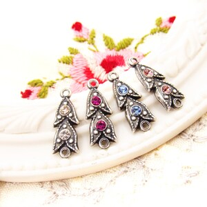May include: Five silver-toned metal charms with a teardrop shape and three crystal rhinestones. The charms are in different colors: clear, pink, light blue, dark blue, and light pink.