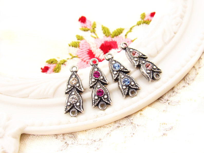 May include: Five silver-toned metal charms with a teardrop shape and three crystal rhinestones. The charms are in different colors: clear, pink, light blue, dark blue, and light pink.