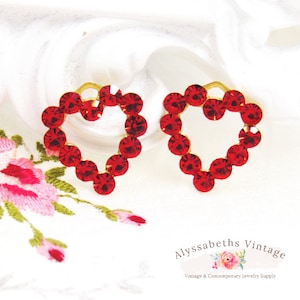 May include: A pair of red heart-shaped earrings with gold settings. Each earring is made of small red rhinestones arranged in a heart shape.