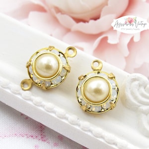 May include: Two gold-tone metal jewelry findings with a round pearl-like bead in the center. Each finding is surrounded by clear rhinestones and has a loop on either side.