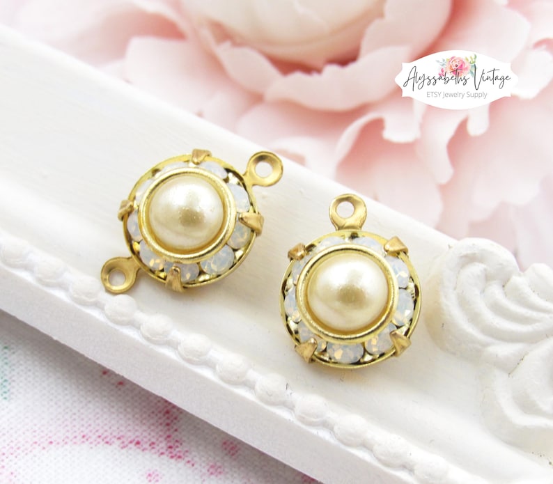 May include: Two gold-tone metal jewelry findings with a round pearl-like bead in the center. Each finding is surrounded by clear rhinestones and has a loop on either side.