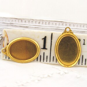 May include: Two gold-toned oval-shaped metal picture frames with a beveled edge. The frames are approximately 1 inch in diameter. One frame has a loop on the top for hanging.