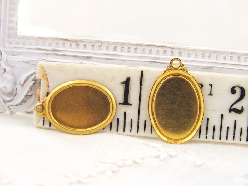 May include: Two gold-toned oval-shaped metal picture frames with a beveled edge. The frames are approximately 1 inch in diameter. One frame has a loop on the top for hanging.
