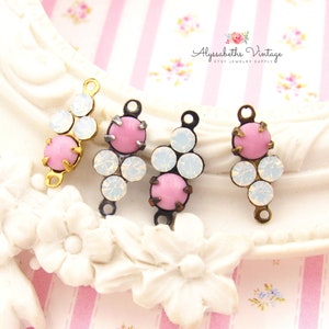 May include: Three gold and silver tone metal connector charms with pink and white rhinestones. The charms are in the shape of a teardrop with three rhinestones on each charm. The charms are for jewelry making.