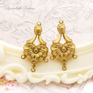 May include: Two gold-tone metal earring findings with a floral design. Each finding has three loops for attaching jewelry components.