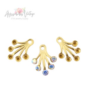 May include: Three gold-toned metal pendant charms with five prongs each. The centre charm has five iridescent clear rhinestones attached to the prongs. The other two charms have five round balls attached to the prongs.