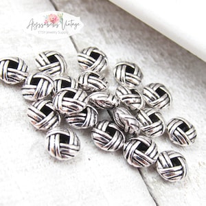 May include: A pile of silver metal beads with a woven design. The beads are round and have a hole in the center. They are perfect for jewelry making.