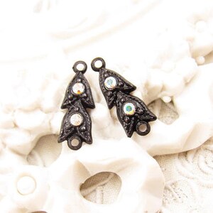 Puede incluir: Dos adornos de metal negro con diamantes de imitaci&oacute;n iridiscentes. Cada adorno tiene forma de hoja estilizada con tres diamantes de imitaci&oacute;n.