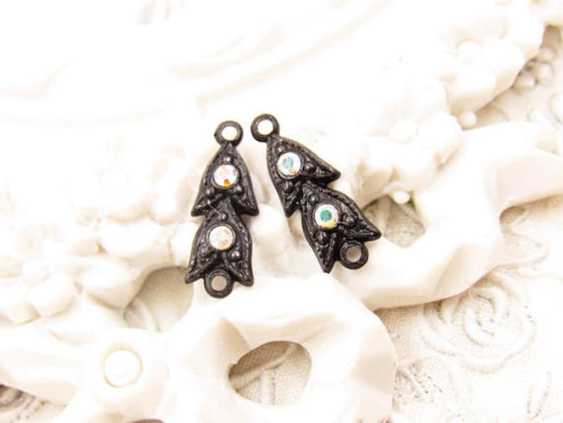 Puede incluir: Dos adornos de metal negro con diamantes de imitaci&oacute;n iridiscentes. Cada adorno tiene forma de hoja estilizada con tres diamantes de imitaci&oacute;n.
