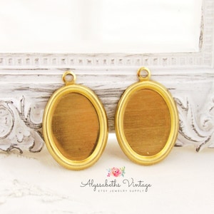 May include: Two gold-toned oval-shaped metal frames with a loop at the top. The frames are blank and ready for a cameo or photo.
