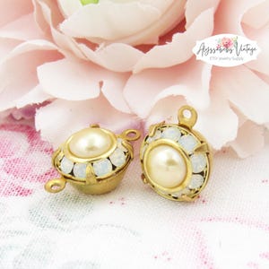 May include: Two gold-tone metal pendant charms with a white pearl center and a halo of white rhinestones.