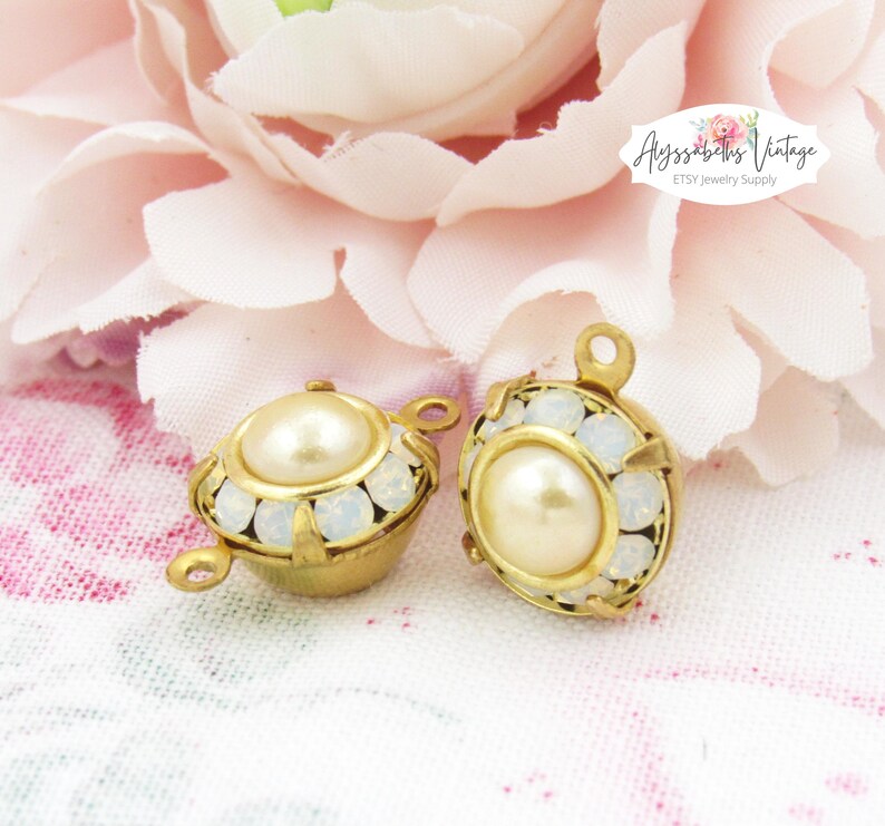 May include: Two gold-tone metal pendant charms with a white pearl center and a halo of white rhinestones.