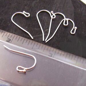 K&ouml;nnte beinhalten: Vier silberne Ohrhaken mit einer kleinen Kugel am Ende jedes Hakens. Die Haken sind etwa 2,5 cm lang und werden neben einem Lineal gezeigt.