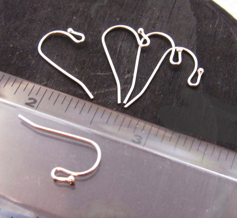 K&ouml;nnte beinhalten: Vier silberne Ohrhaken mit einer kleinen Kugel am Ende jedes Hakens. Die Haken sind etwa 2,5 cm lang und werden neben einem Lineal gezeigt.