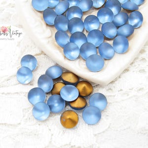 May include: A collection of blue glass beads with a frosted finish, scattered on a white surface. Some beads are a golden color. The beads are in a heart-shaped dish. The Etsy shop name "Alyssabeths Vintage" is visible.