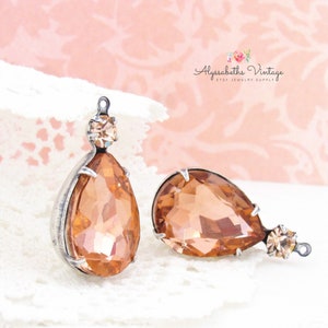 May include: Two teardrop-shaped peach-colored crystal earrings with silver settings. The earrings have a smaller crystal at the top of the teardrop.