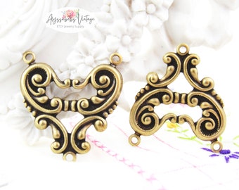 May include: Two antique gold-toned metal connector charms with intricate scrollwork designs. One charm is heart-shaped and the other is a triangular shape. Both charms have three holes for attaching jewelry findings.