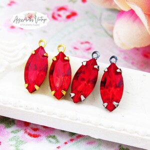 Peut inclure: Quatre cristaux en verre rouge de forme marquise sertis dans des griffes en métal avec de petites boucles au sommet. Deux cristaux sont montés sur des supports en métal doré et deux sur des supports en métal argenté, alignés en rangée.