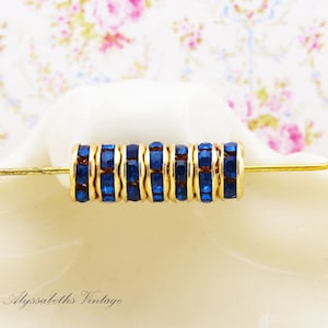 May include: A close-up of a strand of gold-toned bead spacers with blue rhinestone accents. The spacers are strung on a thin wire and are ready to be used in jewelry making.