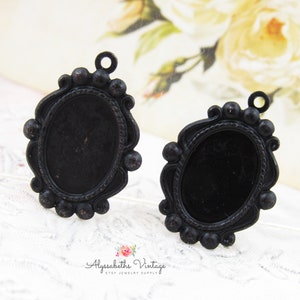 May include: Two black metal oval picture frames with ornate details and a loop at the top for hanging. The frames are blank and ready for a photo or other embellishment.