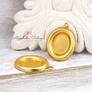 May include: Two gold-toned metal oval pendant trays with a raised edge and a loop for hanging. The trays are blank and ready for embellishment.