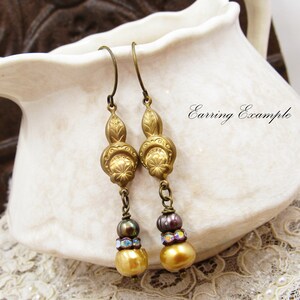 May include: Gold tone earrings with a floral design and three beads, including a gold bead, a dark brown bead, and a clear iridescent bead.