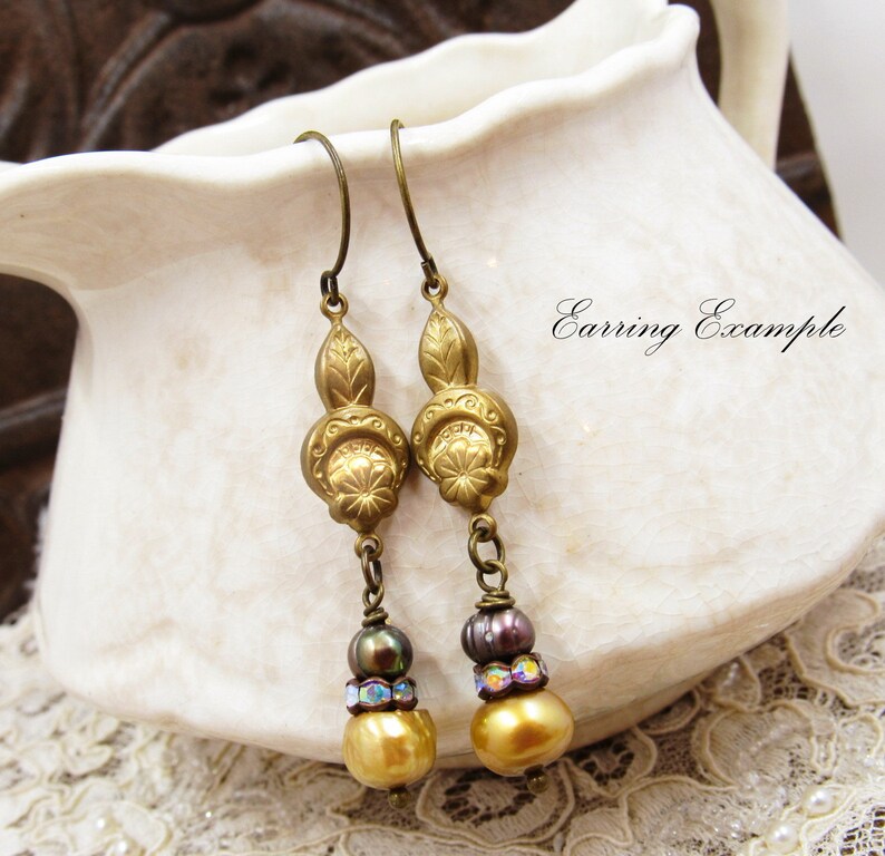 May include: Gold tone earrings with a floral design and three beads, including a gold bead, a dark brown bead, and a clear iridescent bead.