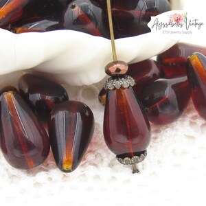 Peut inclure: Un bol de perles en verre rouge fonc&eacute; en forme de larme avec une perle en m&eacute;tal dor&eacute; sur une &eacute;pingle. Les perles sont sur une surface en dentelle blanche. Le texte "Alyssabeths Vintage ETSY Jewelry Supply" est en arri&egrave;re-plan.