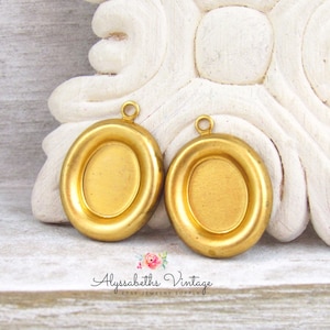 May include: Two gold-toned oval-shaped metal pendant blanks with a smooth surface. The blanks have a raised edge around the perimeter.