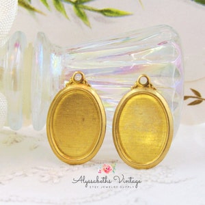 May include: Two gold oval-shaped metal pendant blanks with a brushed finish. The blanks have a loop at the top for attaching a chain or cord.
