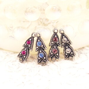 May include: Three silver-toned metal charms with a leaf design and three rhinestones each. The charms have a loop at the top for attaching to jewelry or other crafts. The rhinestones are pink, blue, and clear.