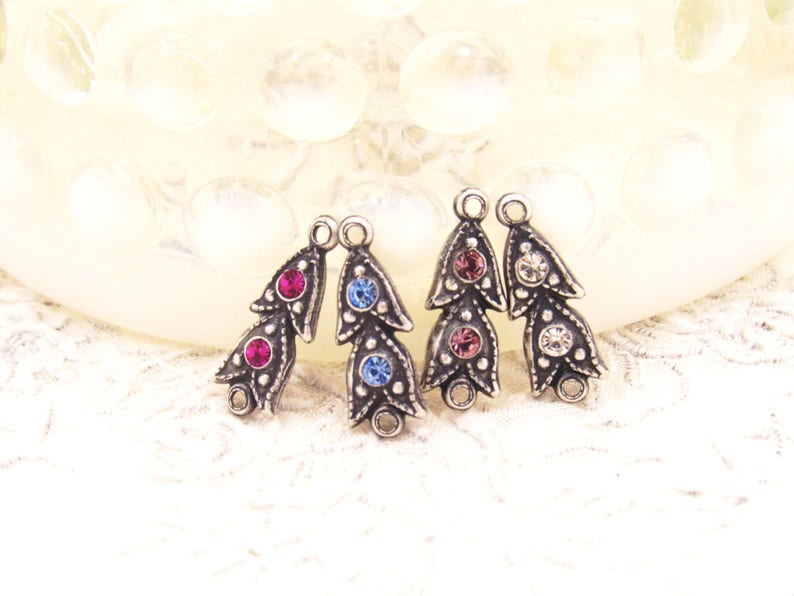 May include: Three silver-toned metal charms with a leaf design and three rhinestones each. The charms have a loop at the top for attaching to jewelry or other crafts. The rhinestones are pink, blue, and clear.