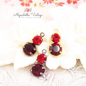 May include: Two pairs of red rhinestone charms with gold and silver settings. The charms are in the shape of a teardrop with two rhinestones.