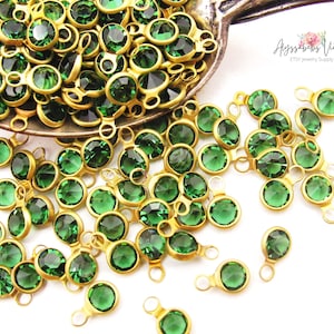 May include: A large quantity of green glass rhinestones with gold-toned metal loops. The rhinestones are scattered on a white surface.