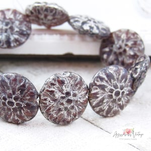 May include: A strand of brown and silver glass beads with a floral design. The beads are round and have a raised design. The beads are strung on a clear string.