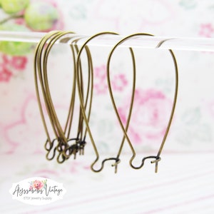 May include: A set of six gold-toned earring hooks, each with a simple, curved shape. The hooks are displayed against a floral background.