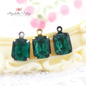 May include: Three emerald green rectangular crystal pendants with metal loops for jewelry making. The pendants are set in silver and gold-toned metal settings. The background is a blurred, off-white surface with the text "Alyssabeths Vintage" and "Etsy Jewelry Supply".