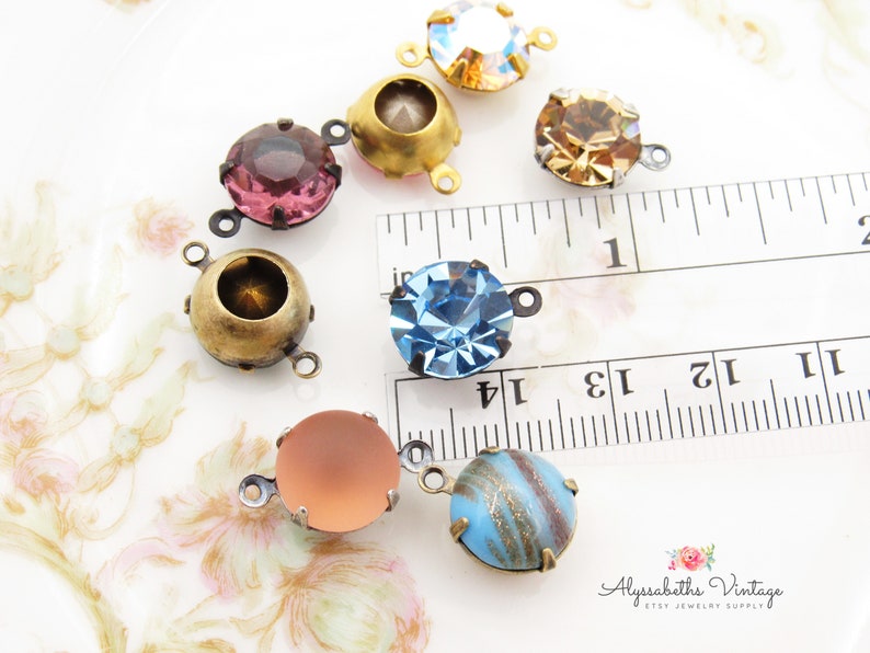 May include: Assortment of colorful glass cabochons with antique brass settings. The cabochons are approximately 1 inch in diameter and have a variety of colors, including pink, blue, and brown. The settings have a loop on each side for attaching to jewelry.