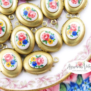May include: Gold-toned oval lockets with floral ceramic inserts. Each locket features a painted design of a red rose, blue and yellow flowers on a white background. The lockets have a small loop for attaching to a chain or bracelet.