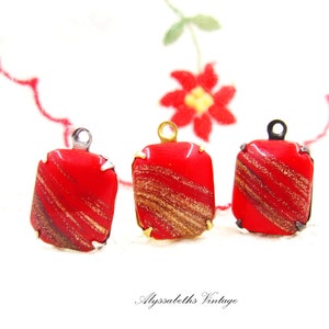 May include: Three red glass pendant charms with gold flecks and silver or black metal settings.
