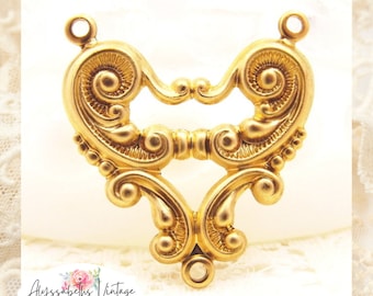 Puede incluir: Un hallazgo de joyería vintage de color dorado con un diseño ornamentado y simétrico. La pieza presenta detalles enrollados, un espacio central abierto y bucles para la fijación. El texto "Alyssabeths Vintage" y "ETSY Jewelry Supply" es visible.
