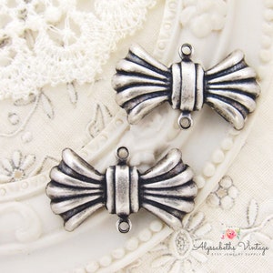 May include: Two silver-toned metal bow-shaped charms with a textured surface. Each charm has two loops for attaching to jewelry or other crafts.