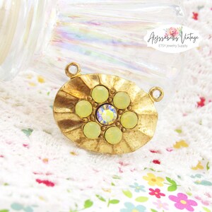 May include: Gold-toned oval pendant with a raised, scalloped edge. The pendant features a cluster of seven pale green rhinestones, with a smaller clear rhinestone in the center.